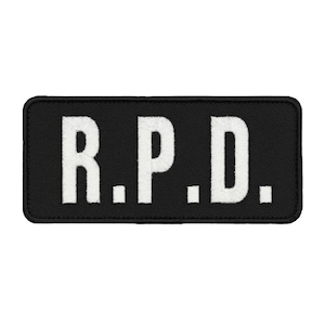 May include: A rectangular embroidered patch with a black background and white stitched lettering that reads R.P.D. The patch features a clean, finished border and is designed for attachment to fabric surfaces through sewing or heat application.