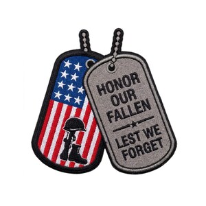 May include: Two embroidered patches shaped like military dog tags. One patch features the American flag with a black silhouette of a helmet, rifle, and boot. The other grey patch displays the black text: HONOR OUR FALLEN LEST WE FORGET.