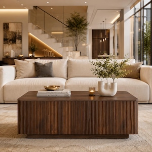 May include: A rectangular coffee table made of dark brown wood with a vertical slatted design on the sides. The table surface holds a stack of two books titled Live Beautiful and Kinfolk, a small gold bowl, a lit candle, and a white ceramic vase.