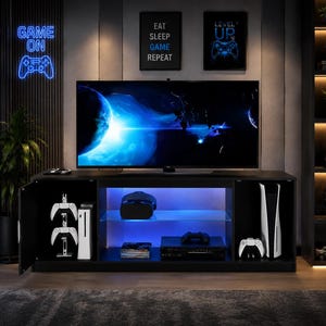 May include: A black media console with three storage sections, featuring blue LED interior lighting, glass shelving, and a large flat-screen television on top. The unit houses gaming consoles, controllers, and media devices in a modern living space.