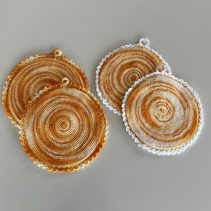 May include: Four handmade crochet coasters. Two sets of two coasters each. The coasters are circular with a spiral design in shades of orange and white. One set has a white scalloped edge.
