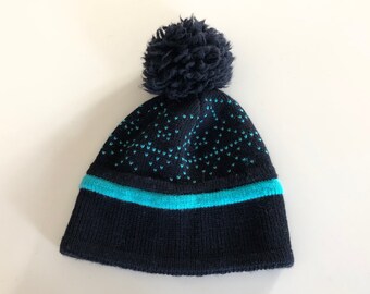 May include: A black knit beanie with a blue stripe and a black pom pom on top.