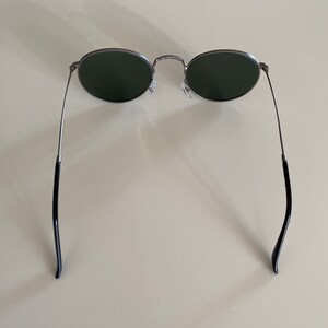 May include: A pair of round, silver-framed sunglasses with dark green lenses. The sunglasses have black arms.