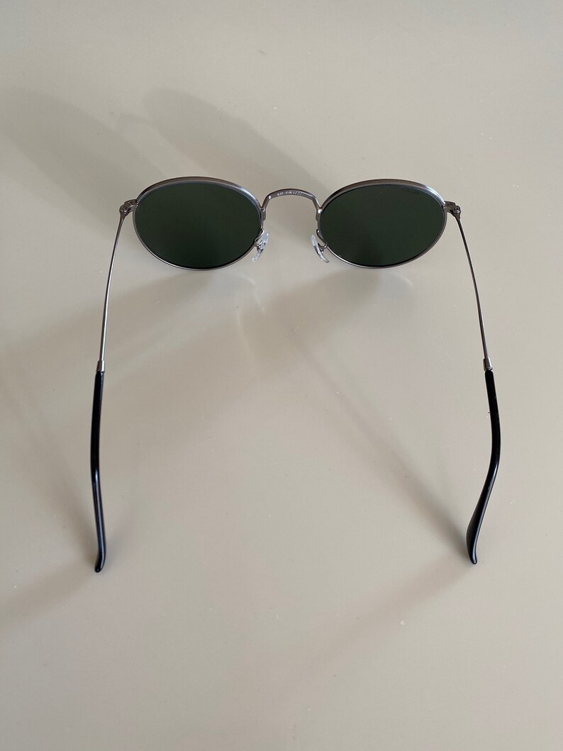 May include: A pair of round, silver-framed sunglasses with dark green lenses. The sunglasses have black arms.