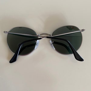 May include: A pair of round, silver-framed sunglasses with dark green lenses. The sunglasses have black arms.