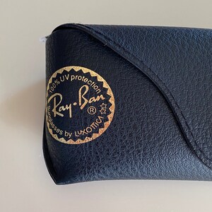 May include: A black leather case with a gold Ray-Ban logo that reads "100% UV protection Sunglasses by Luxottica".
