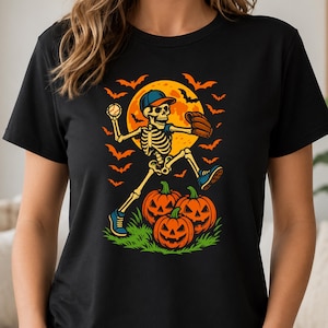 May include: A black t-shirt featuring a graphic of a skeleton wearing a baseball cap and glove, throwing a baseball. The skeleton is positioned above three jack-o'-lanterns on green grass, set against a large yellow moon and orange bats.