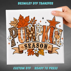 May include: A white DTF transfer sheet featuring the text PUMPKIN SEASON in large block letters with varied patterns including leopard print, orange plaid, and floral designs. The graphic includes orange maple leaves, daisies, and a star.