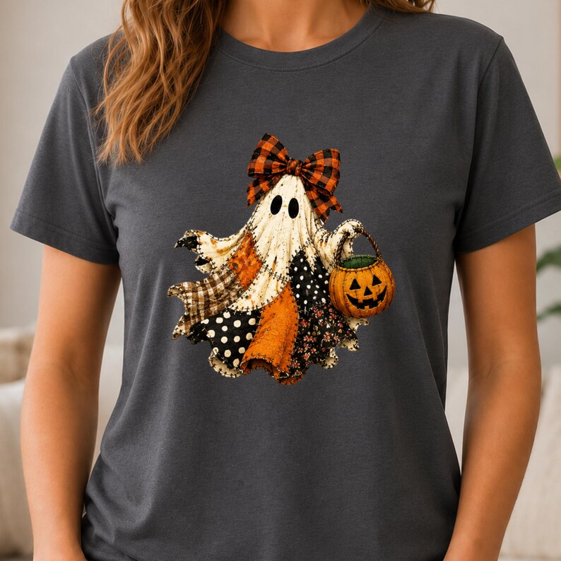 May include: A dark gray short-sleeve t-shirt featuring a graphic of a ghost wearing an orange and black plaid bow. The ghost has a patchwork body with various patterns and holds a small orange jack-o'-lantern bucket with a black face.
