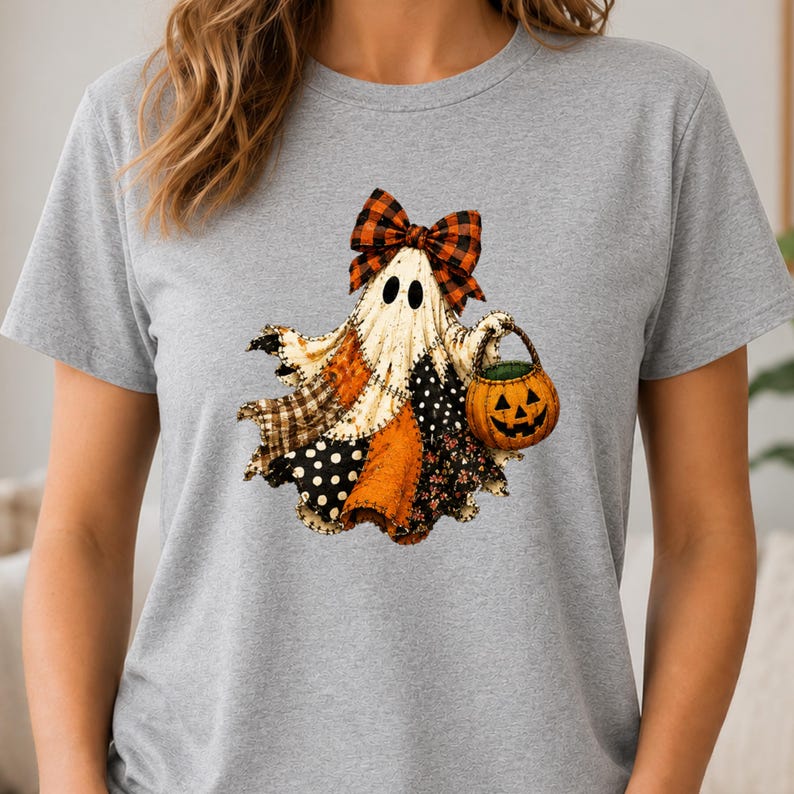 May include: A heather gray t-shirt featuring a graphic of a ghost wearing a plaid bow. The ghost has a patchwork-style body with various patterns including polka dots, plaid, and floral prints. It is holding a small orange jack-o'-lantern bucket.