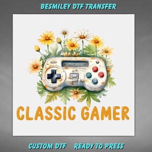 May include: A white video game controller graphic with a distressed texture, surrounded by yellow daisies and green leaves. The text BESMILEY DTF TRANSFER appears at the top, and the text CLASSIC GAMER is printed in orange below the controller.
