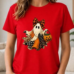 May include: A bright red short-sleeved t-shirt featuring a central graphic of a ghost made of various patterned fabric patches. The ghost wears a plaid bow on its head and carries a small orange jack-o'-lantern bucket with a black face.