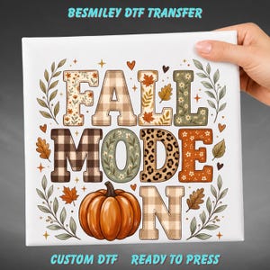 May include: A DTF transfer sheet featuring the text FALL MODE ON with a pumpkin replacing the letter O. The letters feature various patterns including plaid, leopard print, and floral designs, surrounded by autumn leaves and small stars.