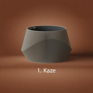 May include: A gray, wide-mouthed planter with a textured, vertically ribbed exterior and a smooth, dark gray interior rim. The vessel features a geometric, faceted silhouette. The text 1. Kaze is printed in white below the object.