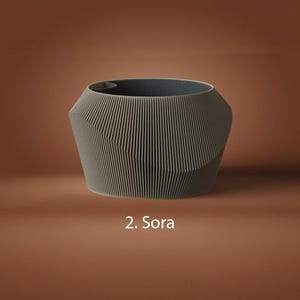 May include: A gray planter with a ribbed, geometric exterior featuring vertical lines and angled facets. The interior is dark gray, and the text 2. Sora is printed in white below the object, which has a wide, open circular top rim.