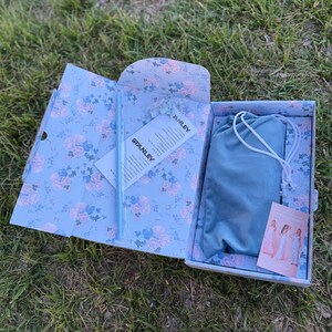 May include: A rectangular gift box with a light blue floral pattern containing a light blue straw, a white Stanley brand information card, a blue drawstring pouch, and a small rectangular card featuring images of a person in a long dress.