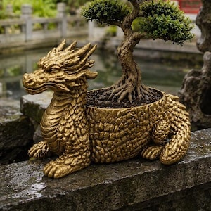 May include: A gold-colored dragon-shaped planter featuring a textured, scale-like surface and a detailed head with horns. The body of the dragon serves as a container holding a small, green, multi-tiered bonsai tree with a gnarled, woody trunk.
