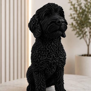 Könnte beinhalten: Eine einfarbig schwarze Skulptur eines sitzenden Hundes mit lockigem, texturiertem Fell. Die Figur zeigt detaillierte Fellstrukturen, Schlappohren und eine ausgeprägte Schnauze, die einen Hund vom Typ Doodle oder Spaniel in sitzender Haltung darstellt.