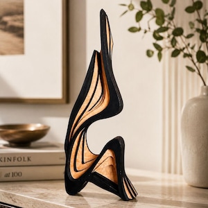 Può includere: Una scultura astratta alta composta da pannelli curvi stratificati. La struttura presenta sezioni alternate di nero opaco e legno chiaro naturale, creando una silhouette dinamica e fluida con spazi aperti tra gli strati sovrapposti.