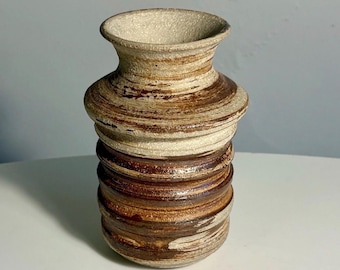 May include: A cylindrical ceramic vase featuring a textured, speckled off-white finish on the flared rim and upper shoulder, transitioning into a series of horizontal, raised ridges with alternating bands of dark brown and cream-coloured glaze.