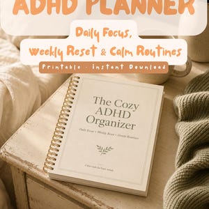 Peut inclure: Un agenda ADHD à reliure spirale avec une couverture crème portant le texte The Cozy ADHD Organizer, Daily Focus, Weekly Reset, Gentle Routines et Calm tools for busy minds. La couverture présente aussi une petite feuille et une bordure.