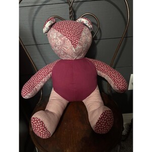 Pode incluir: Um urso de peluche feito de vários retalhos de tecido. A cabeça apresenta uma estampa floral vermelho-escura e um padrão paisley mais claro. O tronco é de cor bordô sólida, enquanto os braços e as pernas são feitos de uma mistura de tecido floral vermelho e tecido xadrez claro.