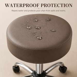 May include: A round, taupe-colored stool seat with a smooth, water-resistant surface featuring visible water droplets. The text WATERPROOF PROTECTION and Repels water and protects your chair from spills and stains is displayed above the seat.