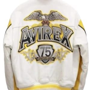 May include: A white and yellow jacket featuring a large embroidered eagle graphic above the text AVIREX. Below the text is a shield emblem with the number 75 and the words AVIATOR'S KING. The jacket has a yellow collar, yellow side panels, and yellow ribbed cuffs.