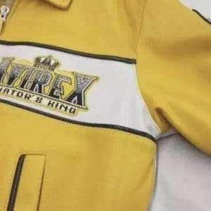 May include: A yellow jacket with a white horizontal chest stripe and a black zipper closure. The chest features an embroidered logo that reads AVIREX AVIATOR'S KING with a crown graphic. The jacket includes a collar and a vertical pocket.