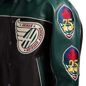 May include: A dark green and black leather jacket featuring a large cream-colored patch on the chest with the text AVIREX HOCKEY DIVISION and winged logo. The sleeve displays two embroidered hockey goalie mask patches with red maple leaves.