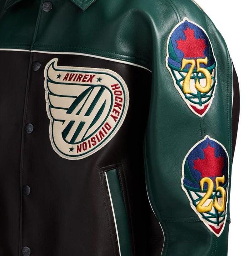 May include: A dark green and black leather jacket featuring a large cream-colored patch on the chest with the text AVIREX HOCKEY DIVISION and winged logo. The sleeve displays two embroidered hockey goalie mask patches with red maple leaves.