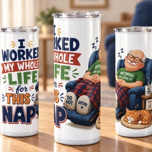 May include: Three white cylindrical tumblers with lids featuring a graphic of a retired person sleeping in a blue armchair with a cat. The text reads I WORKED MY WHOLE LIFE FOR THIS NAP, RETIRED AND LOVIN IT, and DO NOT DISTURB on the slippers.