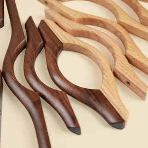 May include: A collection of curved wooden cabinet pulls arranged in a fan pattern. The handles feature a distinct wave-like shape with a central circular cutout. The set includes both dark brown walnut and light tan oak wood finishes.