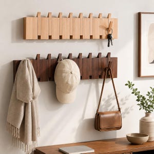 May include: Two horizontal wall-mounted coat racks with retractable wooden hooks. The top rack is light-toned wood, while the bottom rack is dark-toned wood. A beige baseball cap, a beige scarf, and a brown leather handbag hang from the hooks.