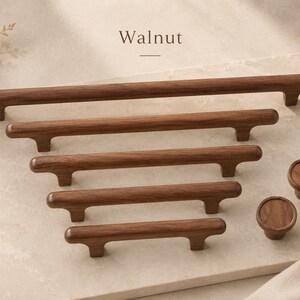 Puede incluir: Una colecci&oacute;n de herrajes para armarios de madera de nogal marr&oacute;n oscuro, que incluye cinco tiradores de barra horizontales de distintas longitudes y dos pomos circulares. La palabra Walnut aparece impresa sobre los herrajes de acabado liso.