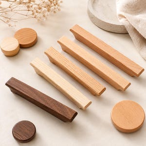 May include: A collection of wooden cabinet hardware including three rectangular drawer pulls and three circular knobs. The items feature various wood tones ranging from light natural grain to dark brown, showcasing smooth surfaces and clean geometric shapes.