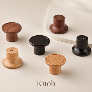 Puede incluir: Una colecci&oacute;n de cinco pomos circulares para armarios en varios acabados de madera, incluyendo roble claro, nogal oscuro y negro. Cada pomo presenta una superficie superior plana, una base cil&iacute;ndrica y un inserto met&aacute;lico central.