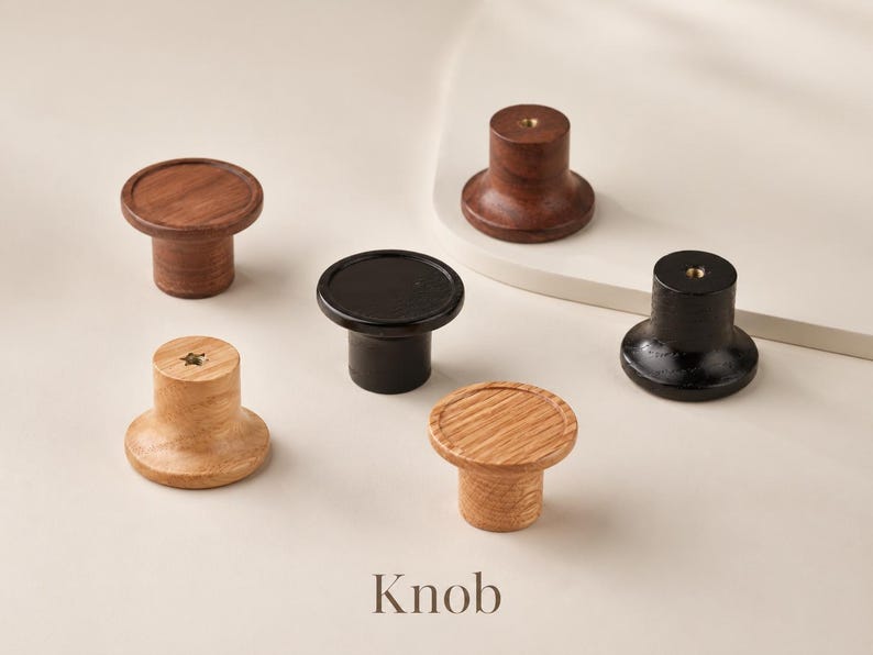Puede incluir: Una colecci&oacute;n de cinco pomos circulares para armarios en varios acabados de madera, incluyendo roble claro, nogal oscuro y negro. Cada pomo presenta una superficie superior plana, una base cil&iacute;ndrica y un inserto met&aacute;lico central.