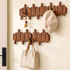 May include: Two horizontal wall-mounted coat racks made of dark brown wooden slats of varying lengths. The top rack holds a beige beret and a set of keys with a small yellow charm. The bottom rack holds a beige handbag with a quilted diamond pattern.