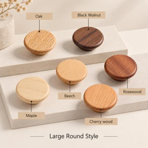 May include: Six round wooden cabinet knobs labeled as Oak, Black Walnut, Beech, Rosewood, Maple, and Cherry wood. The knobs are arranged on two tiered platforms. The text at the bottom reads Large Round Style. Each knob has a distinct wood grain.