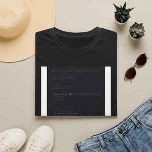 May include: A black short-sleeved t-shirt featuring a rectangular graphic print of computer code on the front. The code snippet is displayed in a dark-themed editor window with white text, including the phrase It works on my machine.