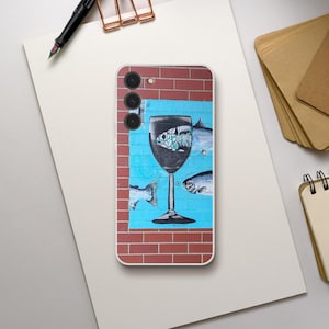 May include: A smartphone case featuring a graphic print of a large wine glass centered on a bright blue background with a red brick pattern border. The design includes illustrations of fish swimming around the glass and a fish skeleton inside.
