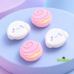 May include: Four silicone thumbstick covers featuring two white cartoon dog faces with blue eyes and pink cheeks, and two pink swirled cinnamon roll designs with yellow accents. The text RetroGrip is printed in the bottom right corner.
