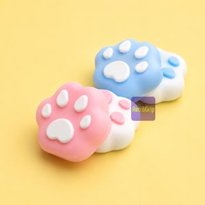 May include: Three paw-shaped thumb grips featuring a pink, blue, and white colour scheme. Each grip has a raised white central pad and four smaller raised white toe pads. A small purple square logo with the text RetroGrip is visible on the side.