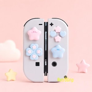 以下が含まれることがあります： パステルカラーのシリコン製ボタンカバーが付いたライトグレーのゲームコントローラー用アタッチメント。カバーにはピンクとブルーの星、ハート、花のデザインが含まれています。右下に黄色でRetroGripという文字が印刷されています。