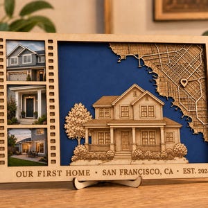 May include: A rectangular wooden frame featuring three vertical photo slots on the left and a laser-cut wooden house model layered over a blue background with a map of San Francisco on the right. Text reads: OUR FIRST HOME • SAN FRANCISCO, CA • EST. 2024.