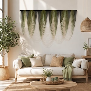 May include: A large wall hanging featuring multiple draped sections of ombre cord that transitions from dark forest green at the top to a light cream color at the bottom, suspended from a horizontal black rod across the wall.