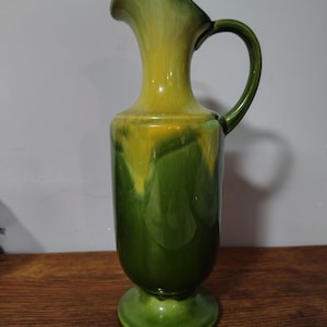 Puede incluir: Una jarra de cerámica alta con un esmalte brillante que presenta un degradado de color desde un verde bosque profundo en la base hasta un amarillo brillante en la parte superior. La jarra tiene un cuello delgado, un asa curva y un pico vertedor.