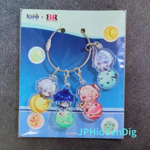 May include: A Genshin Impact and Baskin Robbins collaboration keychain set featuring four clear acrylic charms attached to a silver metal cable ring. Each charm depicts a stylized anime character sitting on a colorful scoop of ice cream.