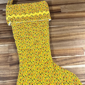 May include: A yellow Christmas stocking with a black and orange floral pattern and a yellow scalloped trim.
